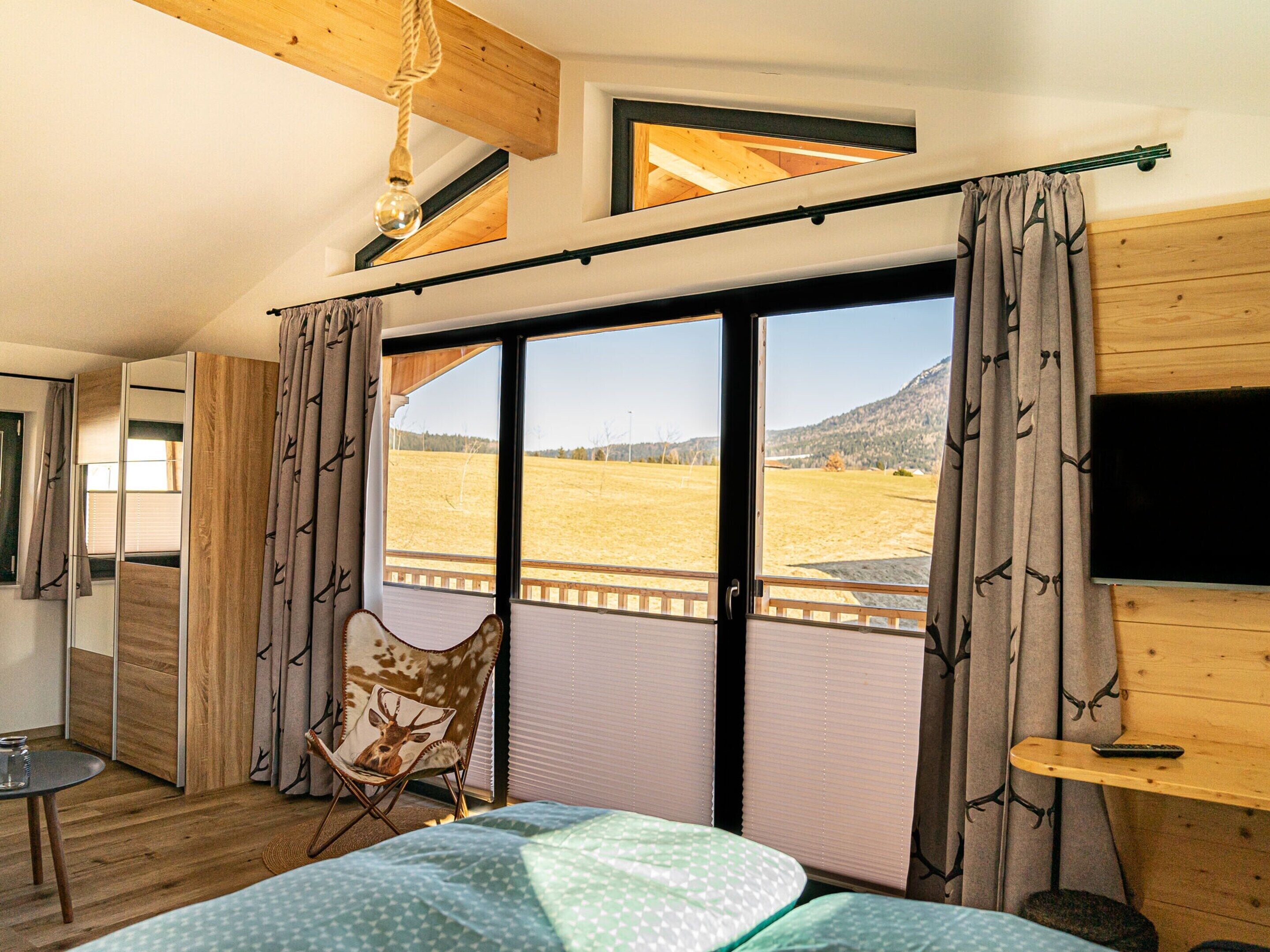 A bedroom with a large sliding glass door leading to a view of a field and mountains.