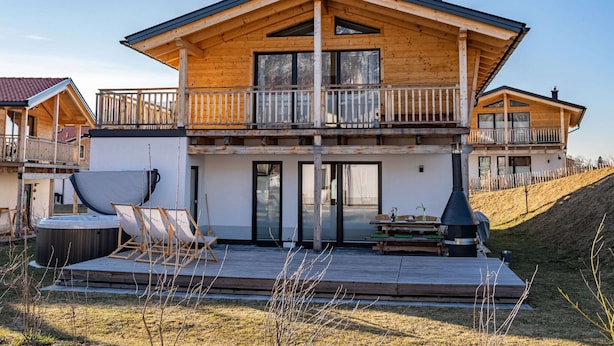 Une maison en bois à deux étages, dotée d’un balcon, d’un jacuzzi et d’un barbecue.