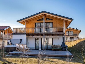 Une maison en bois à deux étages, dotée d’un balcon, d’un jacuzzi et d’un barbecue.