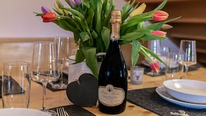 Une bouteille de Prosecco Treviso Extra Dry, bouchée, posée sur une table avec un dessous de verre en forme de cœur, entourée de tulipes et de verres à vin vides.