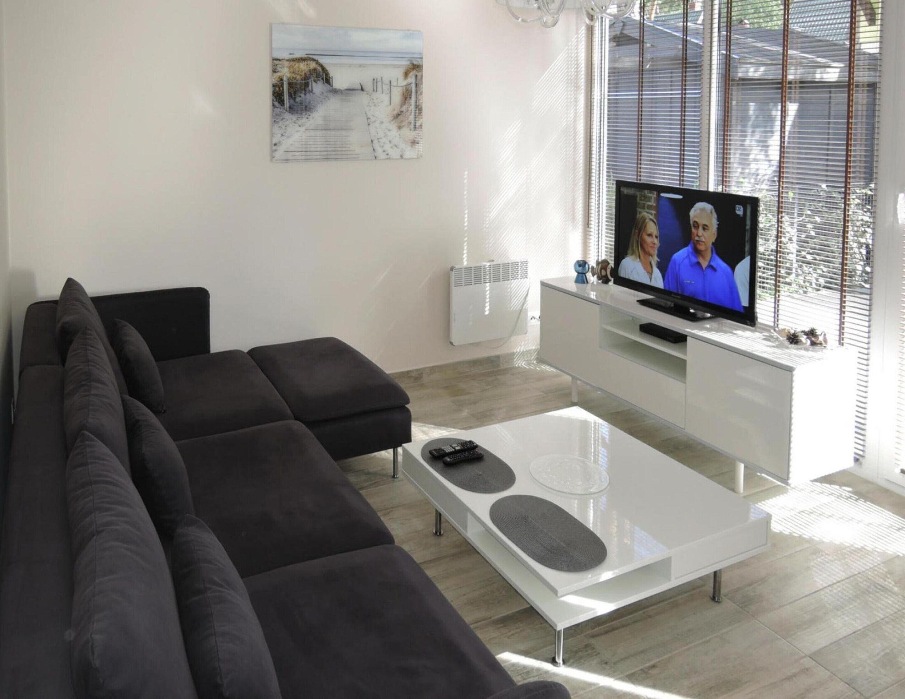 Een moderne woonkamer met een hoekbank, een glazen salontafel en een flatscreen televisie op een witte dressoin.