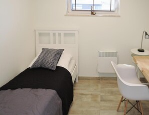 A small, clean room with a bed, a desk, a chair, and a radiator. - Luxury Appartment in Lukecin 60qm (Dziwnów)