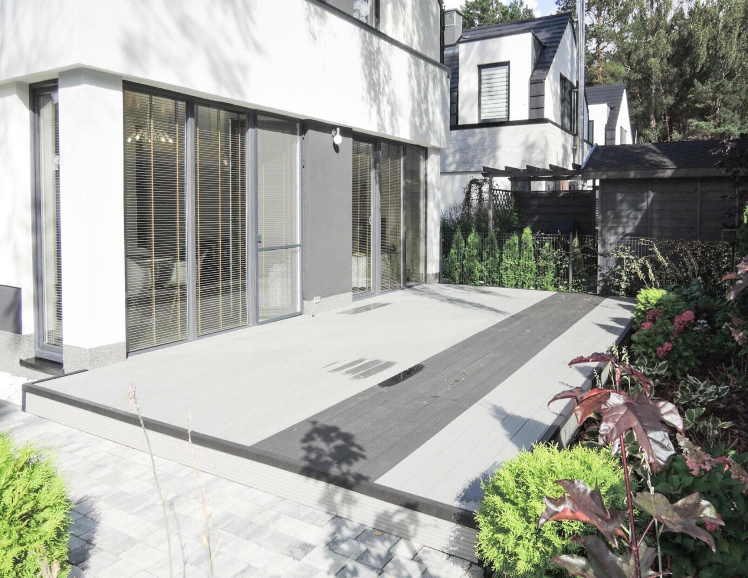 A modern house with large sliding glass doors, a covered patio, and a well-maintained garden.
