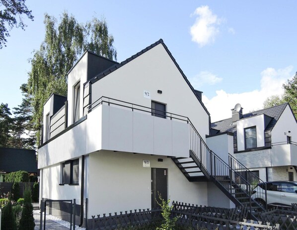 A modern two-story building with a white facade, a black roof, and a visible staircase leading to the upper floor. - Luxury Appartment in Lukecin 60qm (Dziwnów)