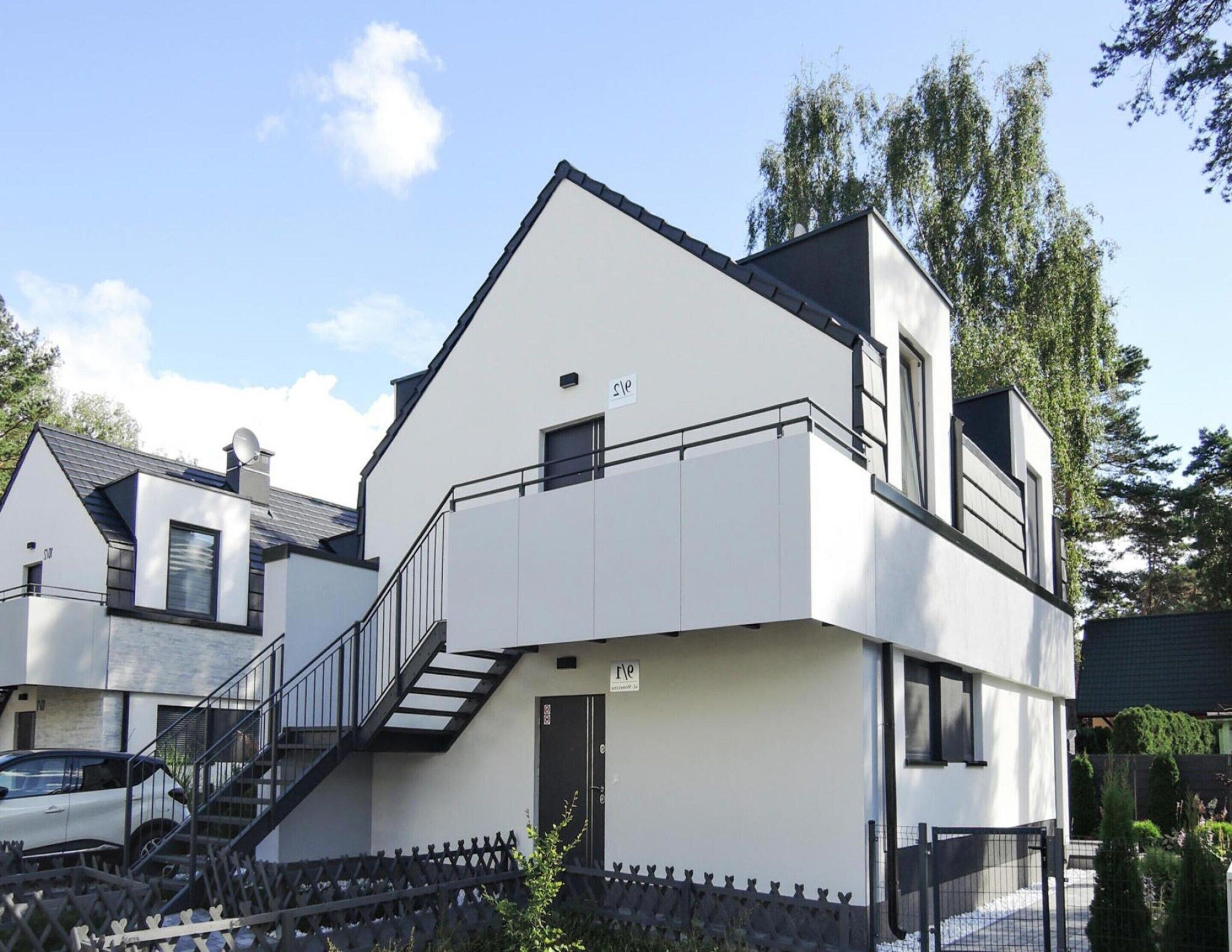 A modern two-story building with a white facade, a balcony on the upper floor, and a staircase leading to the entrance.