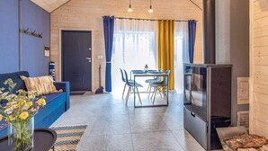A cozy room with a blue sofa, a dining table with chairs, a fireplace, and a window with curtains. - Holiday Cottages Close to the Beach, Jaroslawiec (Postomino)