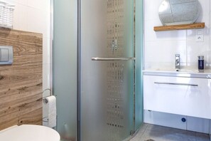 A modern bathroom with a glass shower enclosure, a wooden wall, and a white sink with a mirror above it. - Holiday Cottages Close to the Beach, Jaroslawiec (Postomino)