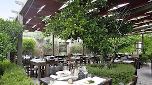 Ein Essbereich im Freien mit Holztischen und -stühlen, umgeben von Grünpflanzen und einem hölzernen Pergola.