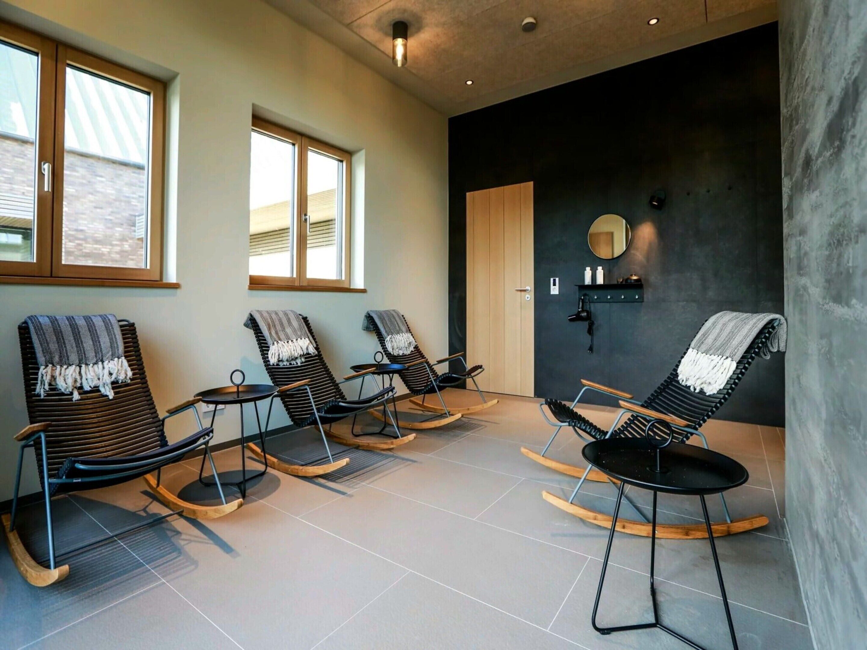 A spa room with four rocking chairs, a wooden door, and a wall-mounted shelf with bottles.