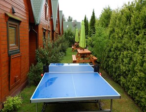A ping pong table in a garden with wooden benches and green umbrellas.