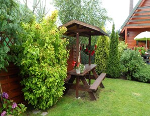 A wooden gazebo with a bench, surrounded by lush greenery and flowering plants.