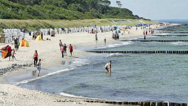 A beach with people walking and standing near the water, tents, and beach chairs. - Ferienwohnung, Ribnitz-damgarten (Ribnitz-Damgarten)