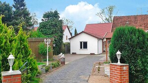 A residential street with a paved road leading to a white house with a red roof. There are two white street lamps on either side of the road, and a brick wall on the left. - Ferienwohnung, Ribnitz-damgarten (Ribnitz-Damgarten)