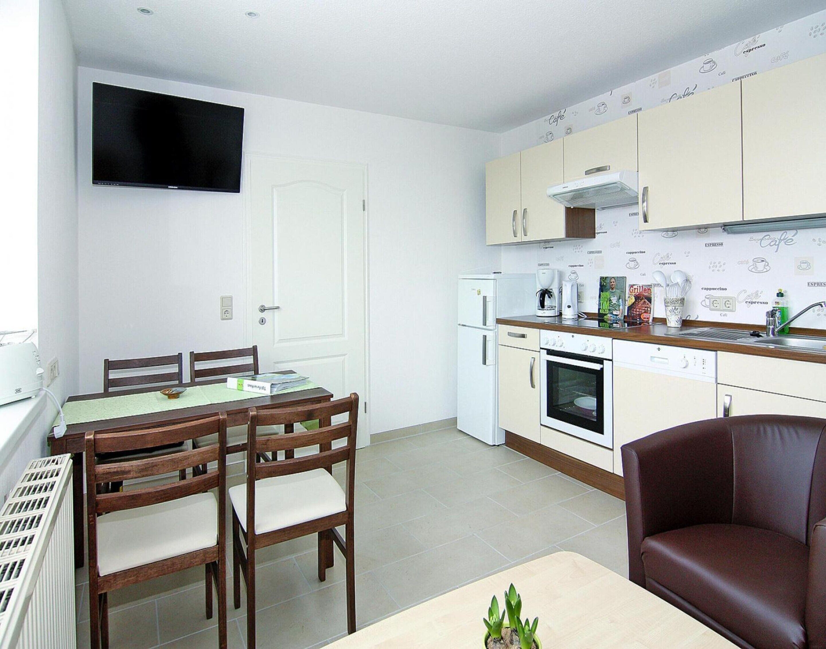 A compact kitchen with a dining area, including a TV mounted above the counter, a coffee maker, and a book on the table.