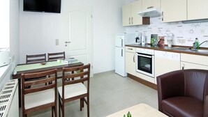 A compact kitchen with a dining area, including a TV mounted above the counter, a coffee maker, and a book on the table. - Ferienwohnung, Ribnitz-damgarten (Ribnitz-Damgarten)