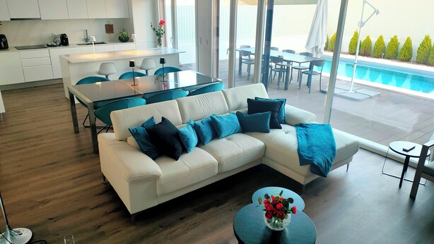 Een moderne woonkamer met een witte bank, een eettafel en uitzicht op een zwembad.