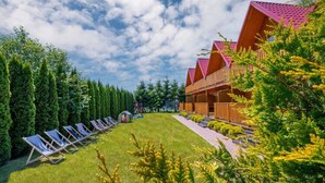 A modern building with a red roof and wooden exterior, surrounded by a well-maintained lawn and rows of sun loungers. - Comfortable Holiday Cottages, Jaroslawiec (Postomino)