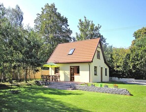 Ein eingeschossiges Haus mit geneigtem Dach, einer Veranda mit Tisch und Stühlen sowie einem kleinen Garten mit Stufen zum Eingang.