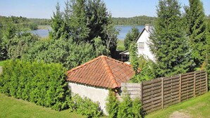 A house with a red-tiled roof, surrounded by dense greenery and a wooden fence. - Holiday Home by Lake Wilkasy With Rowboat (Gizycko)