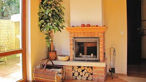 A room with a fireplace, a large potted plant, a basket, and a clock on the wall. - Holiday Home by Lake Wilkasy With Rowboat (Gizycko)