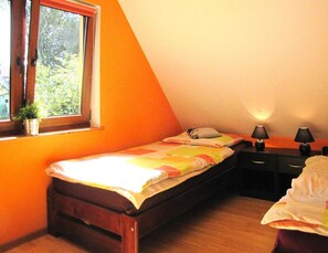 Ein kleines Zimmer mit einem Einzelbett, einem Fenster, einem Nachttisch mit Lampen und einem Blumentopf.