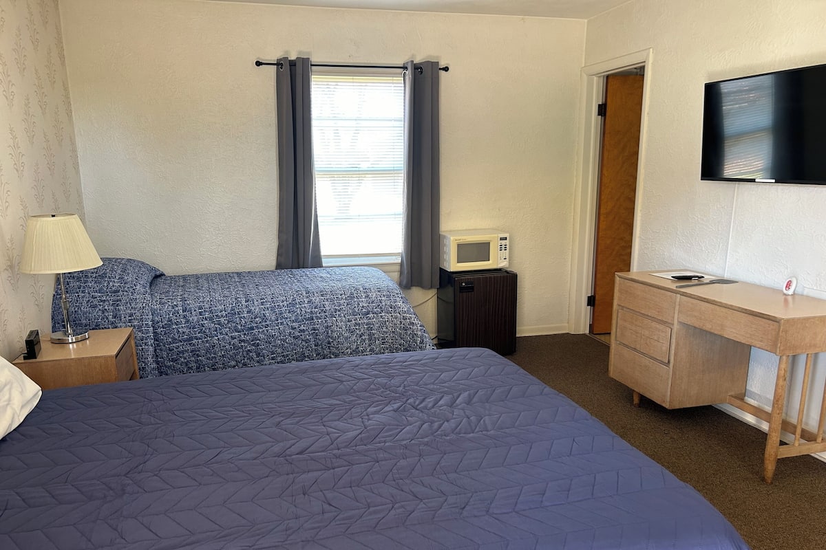 A bedroom with a bed, a desk, a TV, a microwave, and a nightstand.