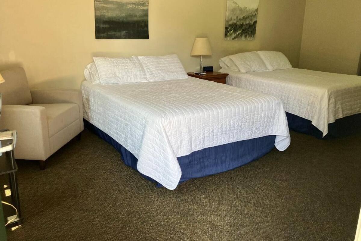 A hotel room with two beds, a chair, a lamp, and artwork on the walls.