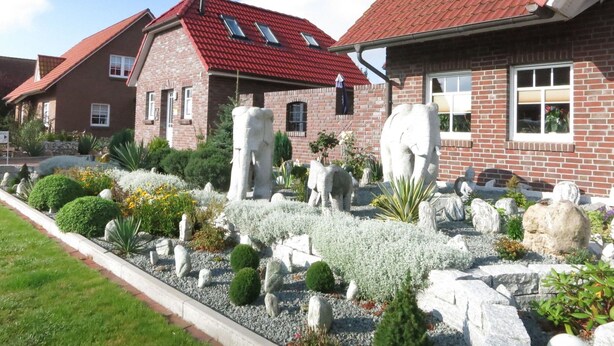 Un quartier résidentiel avec des maisons en briques, un jardin agrémenté de sculptures et un ciel dégagé.