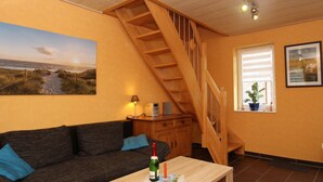 Un salon chaleureux avec un escalier en bois, un canapé, une table basse et un tableau représentant une scène de plage.
