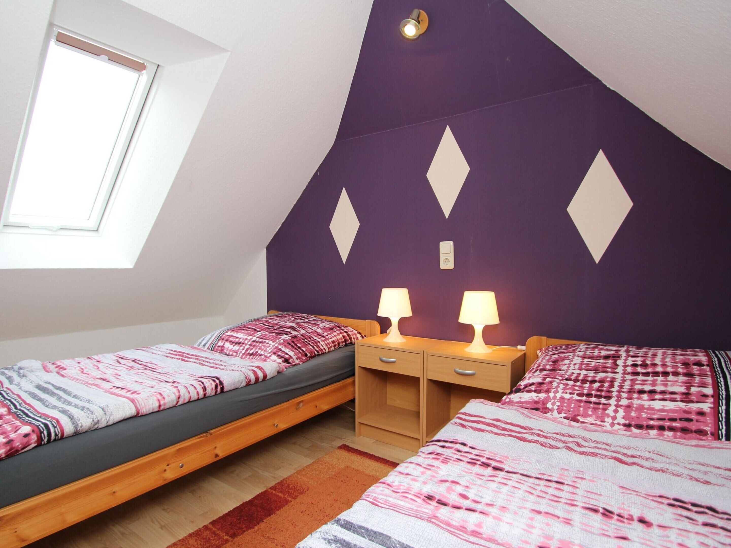 Une chambre avec deux lits simples, une table de chevet en bois, un bureau et une fenêtre.