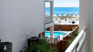 A balcony with a view of a beach, a pool, and a wooden fence.
