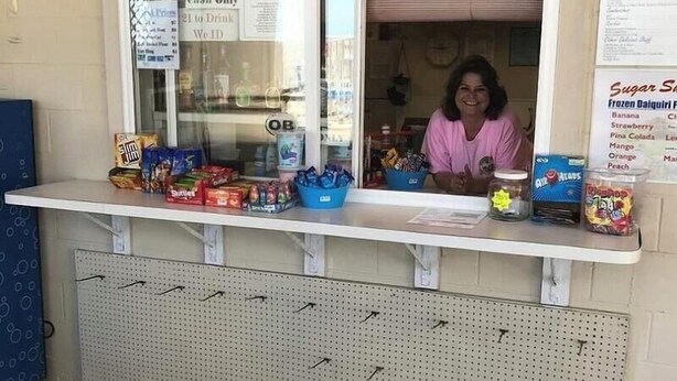 A Sugar Shack with a cash-only policy, a window displaying various snacks, and a menu board listing items like frozen daiquiri flavors.