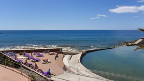 Un resort costero con zona de piscina, sillas de descanso y vistas al océano.