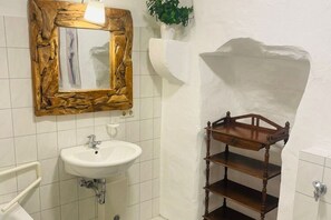 Een badkamer met een witte wastafel, spiegel met houten lijst en een houten plankunit.