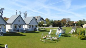 A residential area with white houses, a playground, and a well-maintained lawn. - Comfortable Holiday Homes With Terraces (Ustronie Morskie)