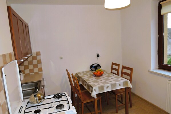 A compact kitchen with a gas stove, wooden chairs, and a table with a checkered tablecloth. - Holiday Home Kolczewo Near Baltic Sea Beach (gmina Wolin)
