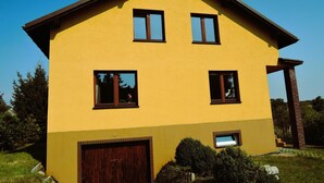 A two-story yellow house with a brown roof, a wooden garage door, and a brick chimney. - Holiday Home Kolczewo Near Baltic Sea Beach (gmina Wolin)