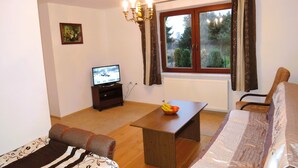 A living room with a sofa, a table with a fruit bowl, a TV, and a window with curtains. - Holiday Home Kolczewo Near Baltic Sea Beach (gmina Wolin)
