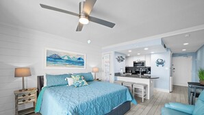 Une chambre à coucher moderne avec un grand lit, un ventilateur de plafond et une vue sur la cuisine.
