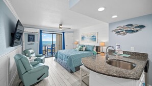 Une chambre avec un lit, un coin salon avec un fauteuil, un lavabo et une vue sur l’océan.