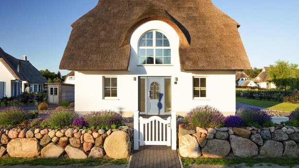 Een wit huis met rieten dak, een centraal rondboogvenster en een witte poort.