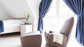 Een slaapkamer met een bed, nachtkastje, stoel en raam met gordijnen.