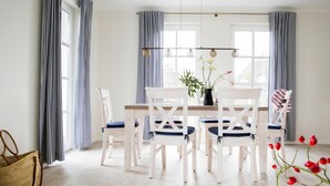 Een eetgedeelte met een witte tafel en stoelen, een vaas met bloemen en een mand op de vloer.