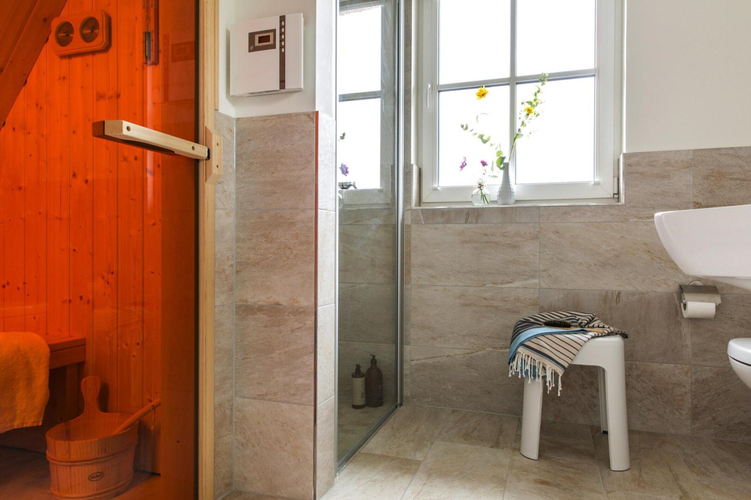 A bathroom with a wooden door, a glass shower enclosure, a white toilet, and a small stool with a towel.