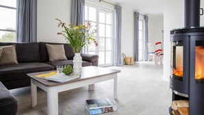 Een woonkamer met een bank, een salontafel met boeken en een vaas, een open haard en een raam met gordijnen.