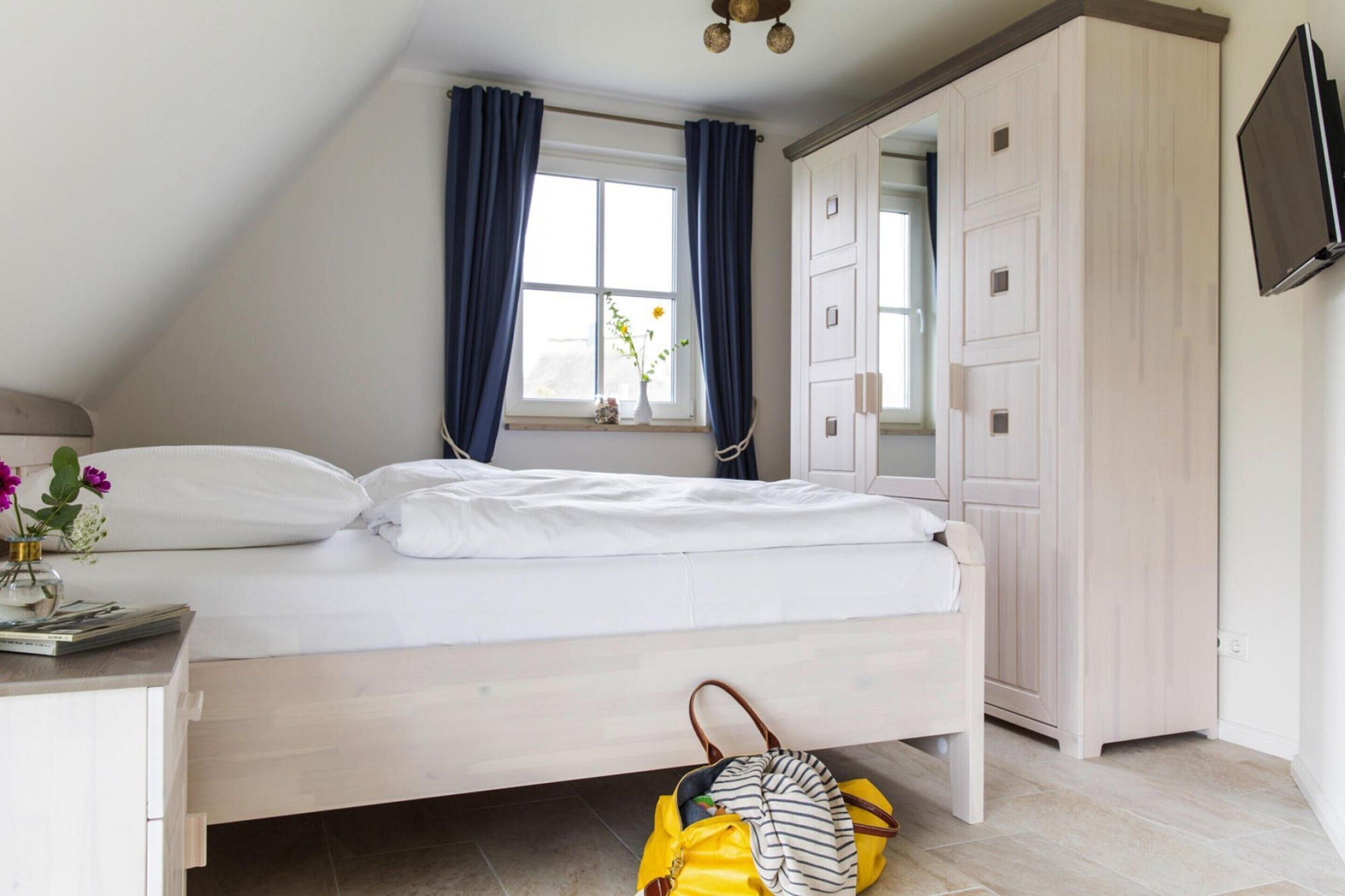 Un dormitorio con cama, armario, escritorio con lámpara y ventana con cortinas.
