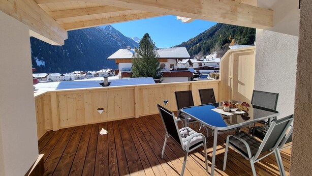 A wooden deck with a table and chairs, overlooking a mountainous landscape. - Panorama Apartment Stubai (Neustift Im Stubaital)