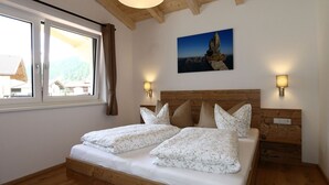 A bedroom with a wooden bed, two bedside tables, a window with curtains, a painting on the wall, and a wooden ceiling. - Panorama Apartment Stubai (Neustift Im Stubaital)