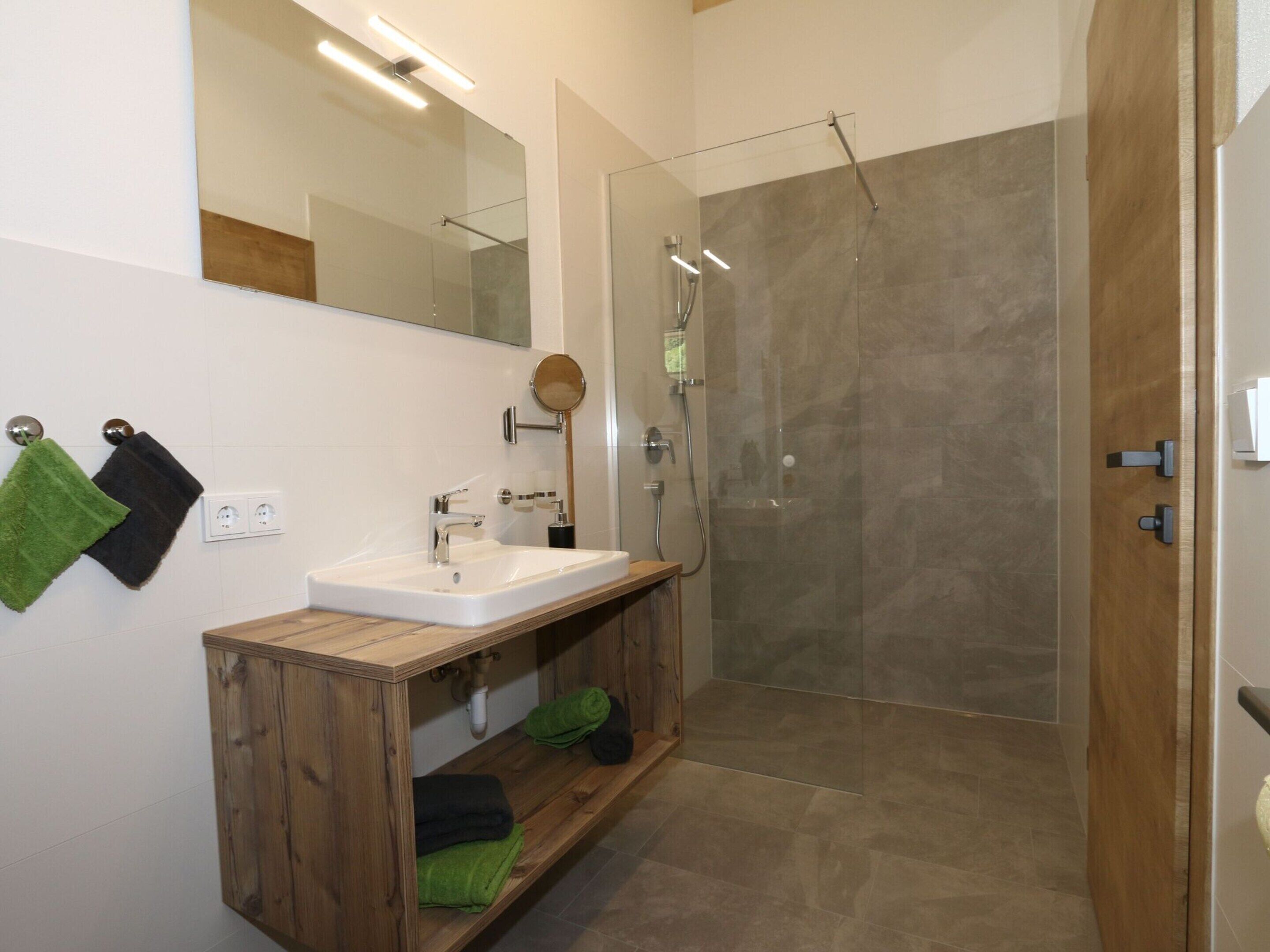 A modern bathroom with a wooden vanity, a glass shower enclosure, and a large mirror.