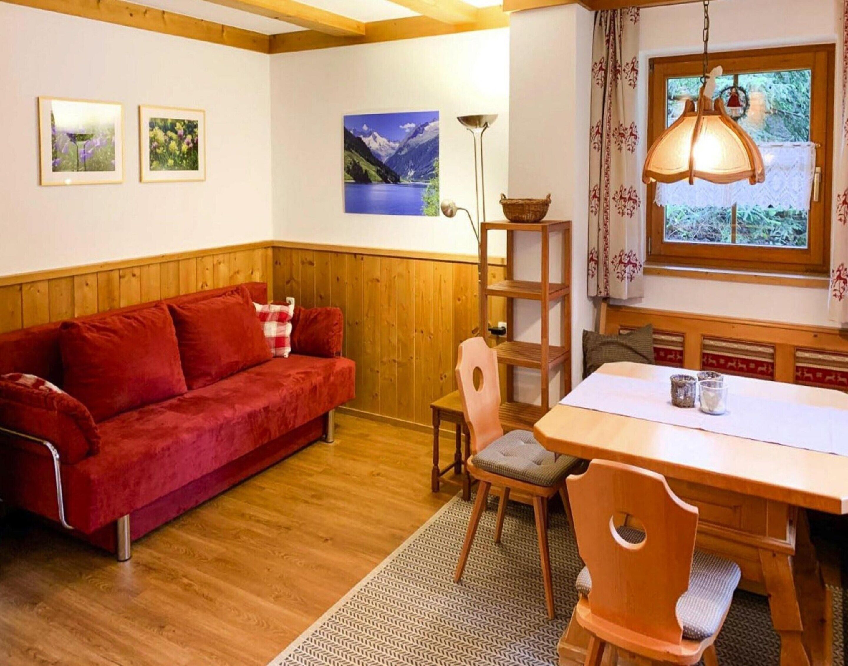 Una habitación acogedora con un sofá rojo, una mesa de comedor de madera, sillas y una lámpara.